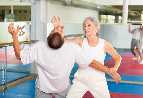 Senior European woman learning chin strike move on man during self-defense training.