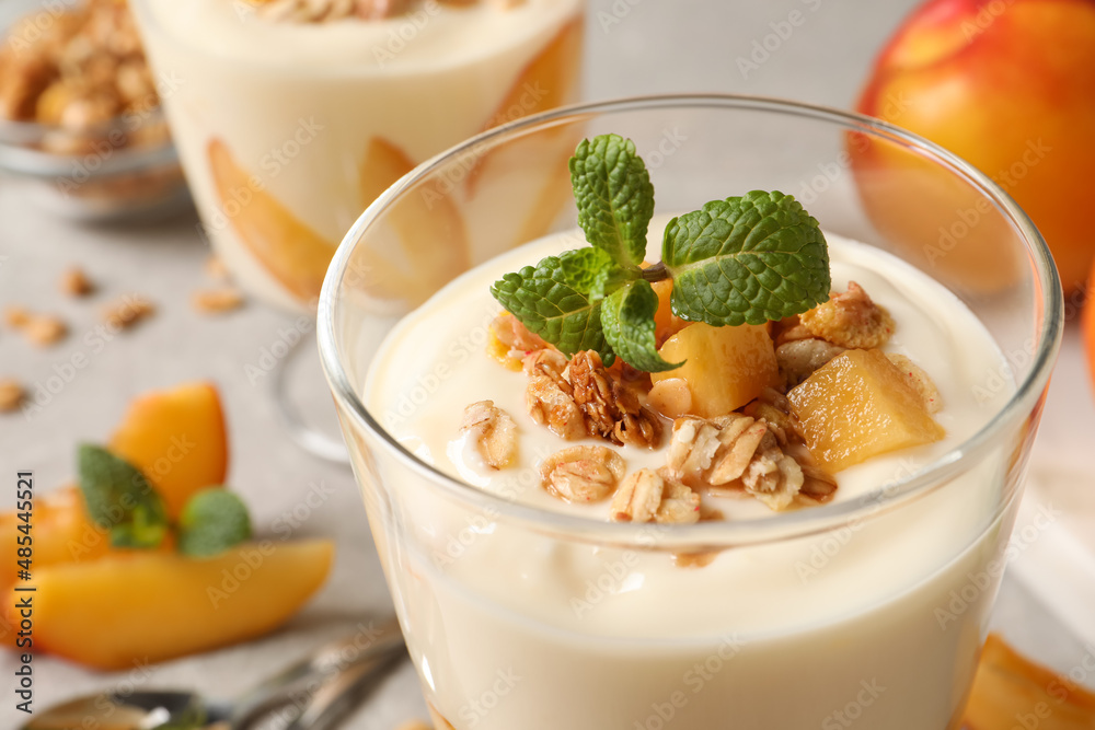Tasty peach yogurt with granola, mint and pieces of fruit in glass on table, closeup Tasty peach yogurt with granola, mint and pieces of fruit in glass on table, closeup
