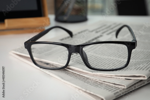 Stack of newspapers and glasses on white table indoors, closeup