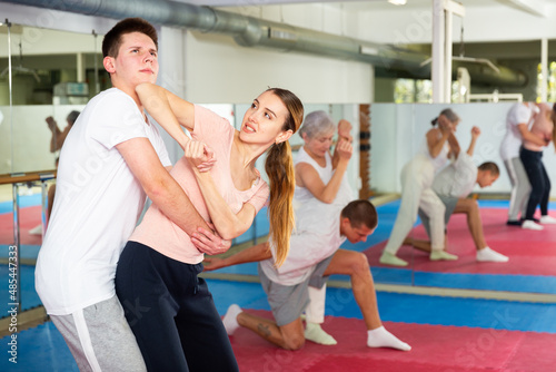 Caucasian woman performing elbow strike while sparring with teenage boy in gym during self-defence training.
