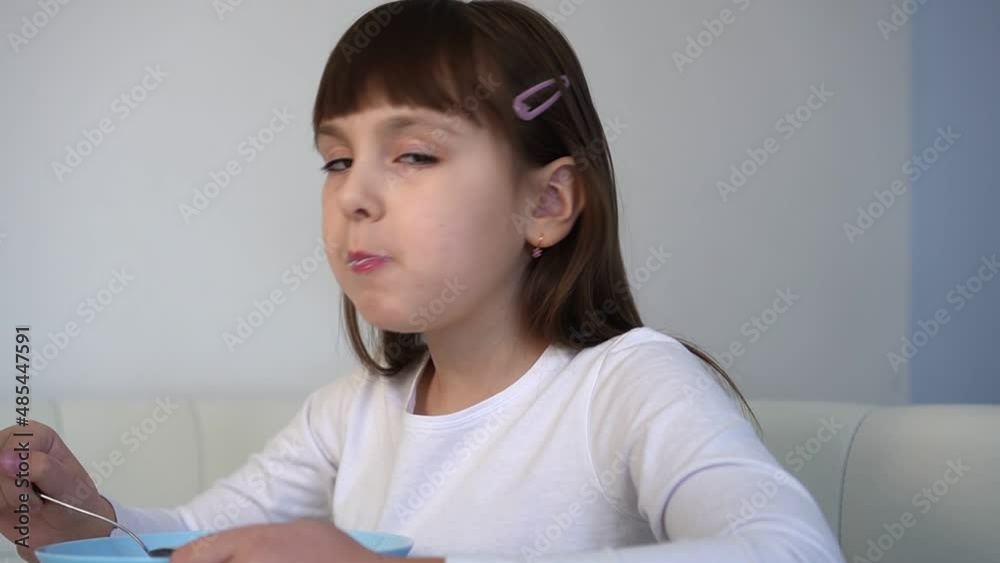 Little girl eats chocolate corn balls with milk sitting at white table. Child have breakfast Little girl eats chocolate corn balls with milk sitting at white table. Child have breakfast
