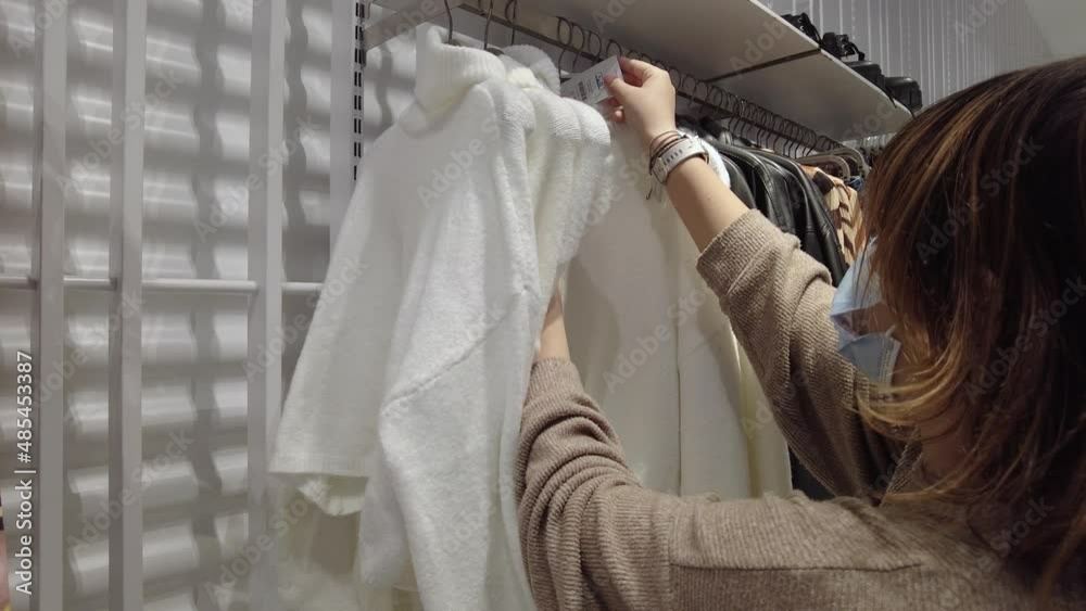 A teen shopping for clothes checks the price tags for sales. A teen shopping for clothes checks the price tags for sales.