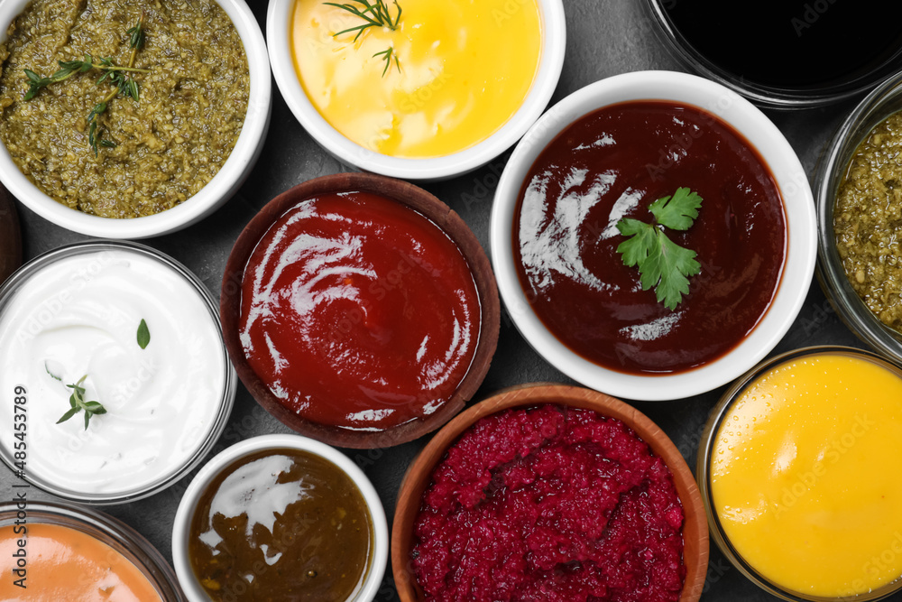 Many different sauces and herbs on black table, flat lay Many different sauces and herbs on black table, flat lay
