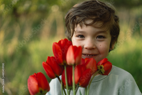Cheerful happy child with tulips flower bouquet in nature. Smiling little boy on nature. Mother's Day, March 8, International Women's Day concept