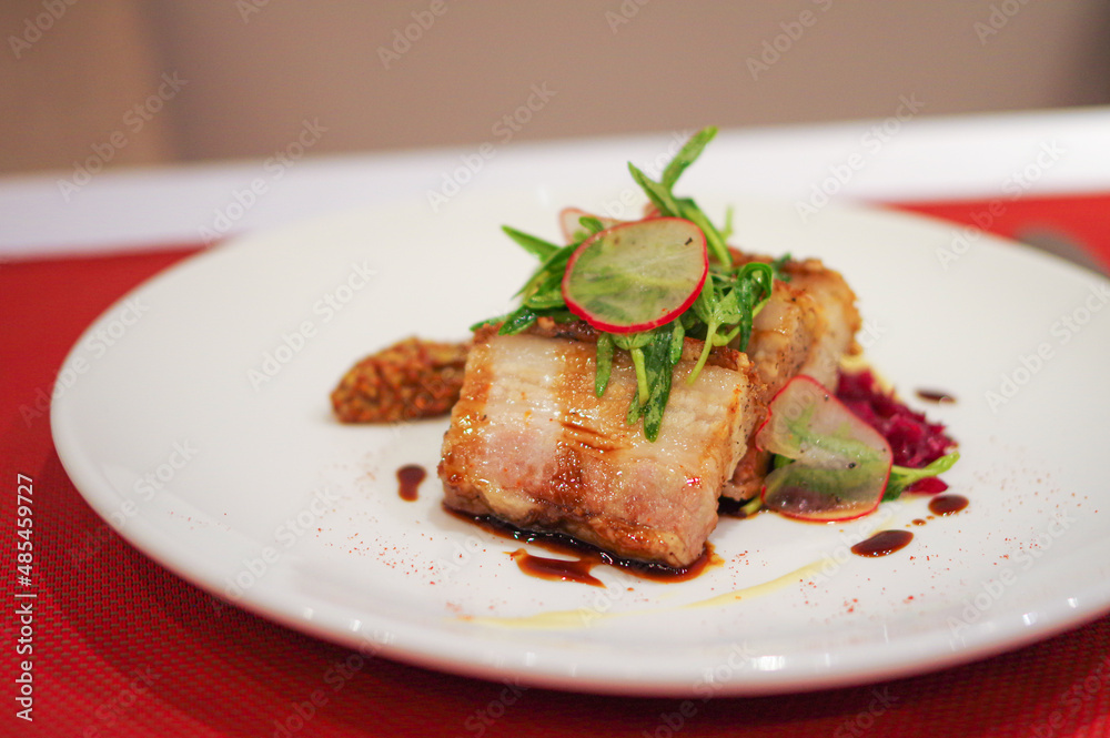 Sliced crispy roasted pork belly with sauce on white plate at asia fusion dish restaurant Sliced crispy roasted pork belly with sauce on white plate at asia fusion dish restaurant