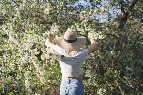 Young beautiful woman in a hat among flowering trees. Spring natural park or garden, flowering trees. Back view. Spring concept © Анастасія Стягайло