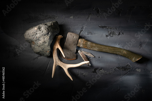 Rugged stone rock with vintage camping hatchet axe and deer antler on textured dark gray surface. photo