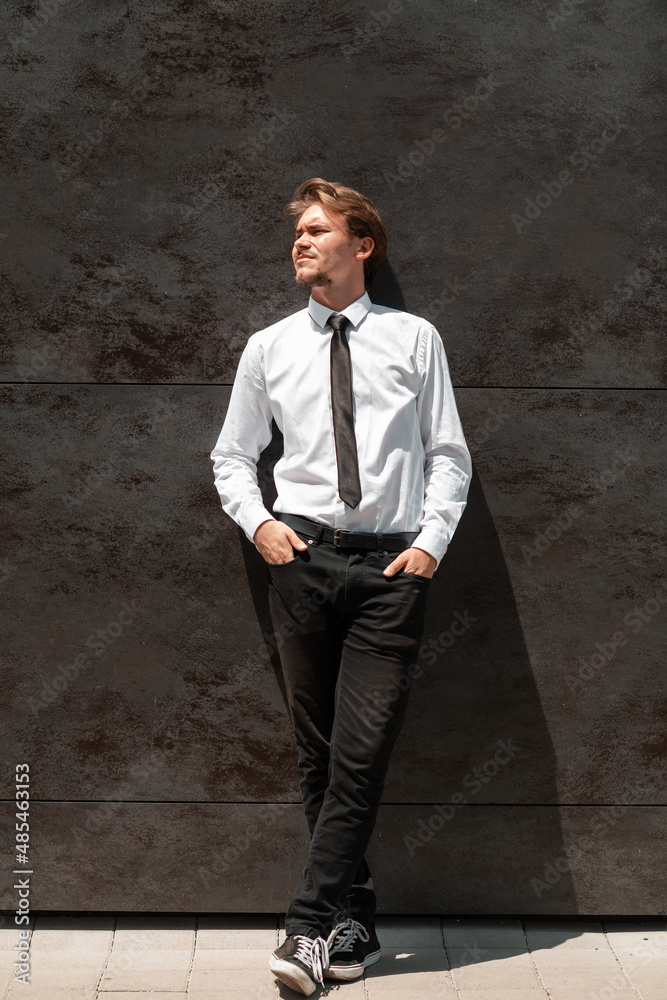 Portrait of startup businessman in a white shirt with a black tie standing in front of gray wall outside Portrait of startup businessman in a white shirt with a black tie standing in front of gray wall outside