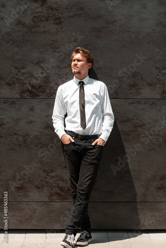 Portrait of startup businessman in a white shirt with a black tie standing in front of gray wall outside