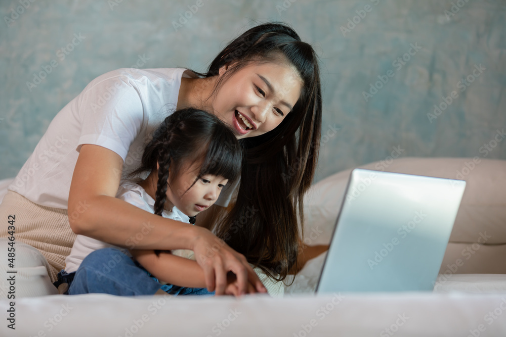 Beautiful Asian mom teaching her daughter to learn and using computer laptop for preschool or watching cartoons online at home.Happy mother relax with little girl having fun with laptop at home Beautiful Asian mom teaching her daughter to learn and using computer laptop for preschool or watching cartoons online at home.Happy mother relax with little girl having fun with laptop at home
