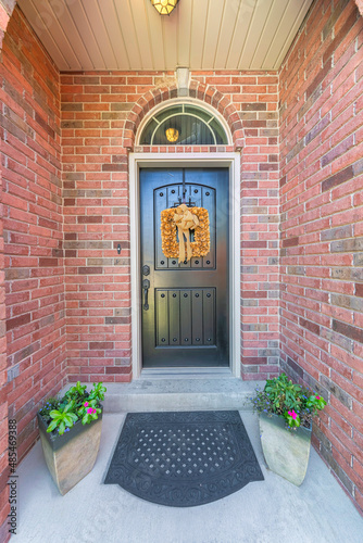 Black front door exterior with yellow wreath and arched transom window