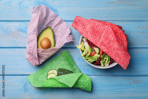 Fotografía Different products in beeswax food wraps on light blue wooden table, flat lay