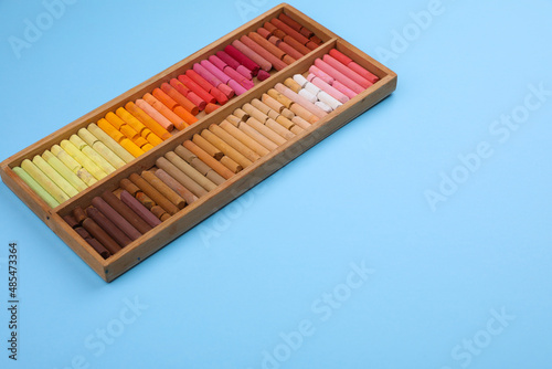 Set of soft pastels in wooden box on light blue background. Drawing material