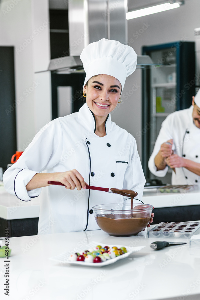 latin woman pastry chef wearing uniform holding a bowl preparing delicious sweets chocolates at kitchen in Mexico Latin America latin woman pastry chef wearing uniform holding a bowl preparing delicious sweets chocolates at kitchen in Mexico Latin America