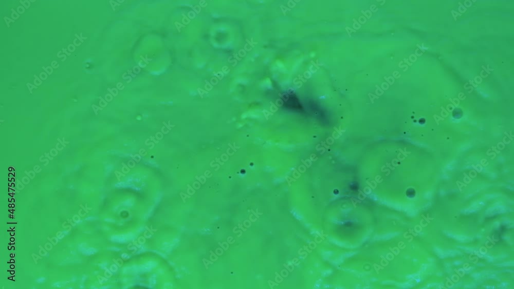 Slow motion. Drops of fluorescent green paint fall down. Splash, spatter and waves of green liquid paint. Top view Slow motion. Drops of fluorescent green paint fall down. Splash, spatter and waves of green liquid paint. Top view