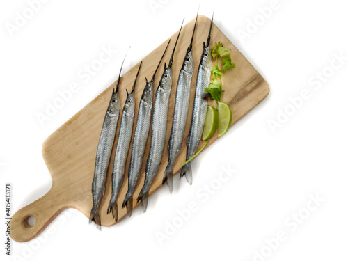 Fresh Ballyhoo halfbeak or Ballyhoo fish (Hemiramphus brasiliensis) is decorated with herbs and vegetables on a wooden pad.Selective Focus. photo