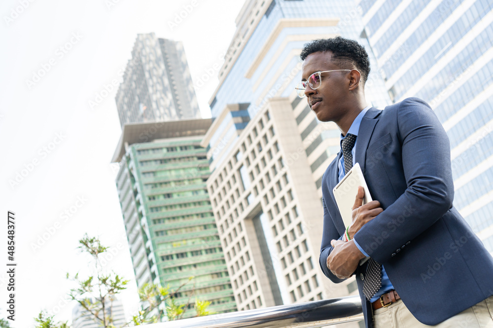 Business people in city. Portrait of an handsome businessman. Modern businessman. Confident young man in full suit and glasses while standing outdoors looking away with cityscape in the background Business people in city. Portrait of an handsome businessman. Modern businessman. Confident young man in full suit and glasses while standing outdoors looking away with cityscape in the background