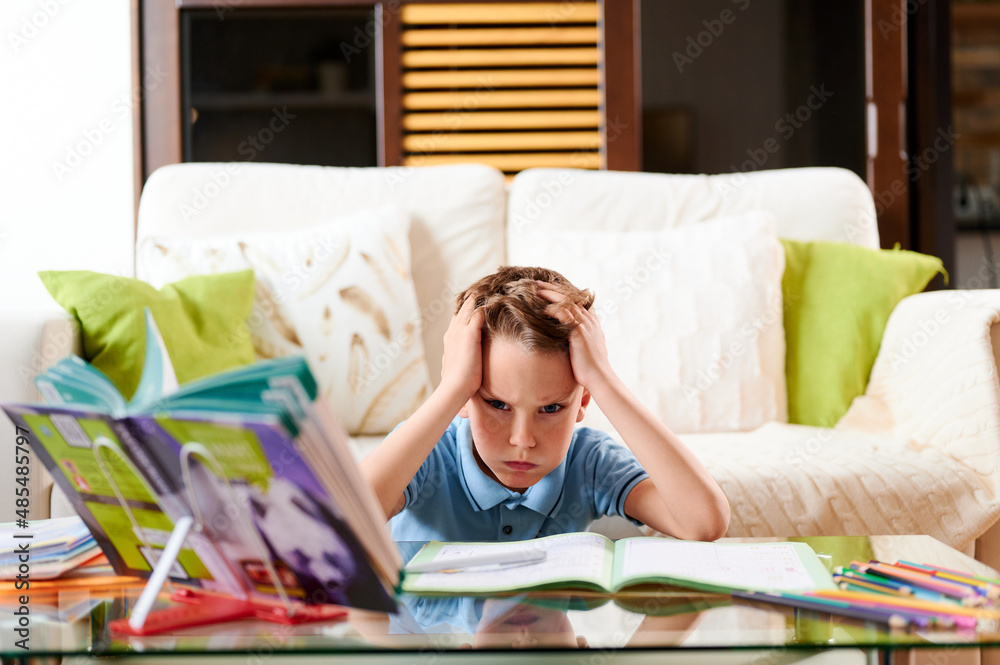 Tired and concentrated boy does homework at home. Homeschooling. Distance learning during quarantine Tired and concentrated boy does homework at home. Homeschooling. Distance learning during quarantine