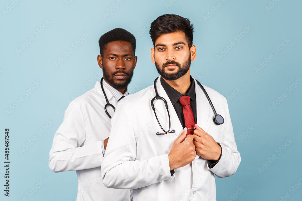 portrait of smiling medical worker in white lab coat with stethoscope conferring with young doctor on blue background portrait of smiling medical worker in white lab coat with stethoscope conferring with young doctor on blue background