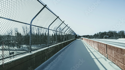 Fototapeta Naklejka Na Ścianę i Meble -  Sidewalk over the highway covered in snow with chain-link fence and concrete barricade