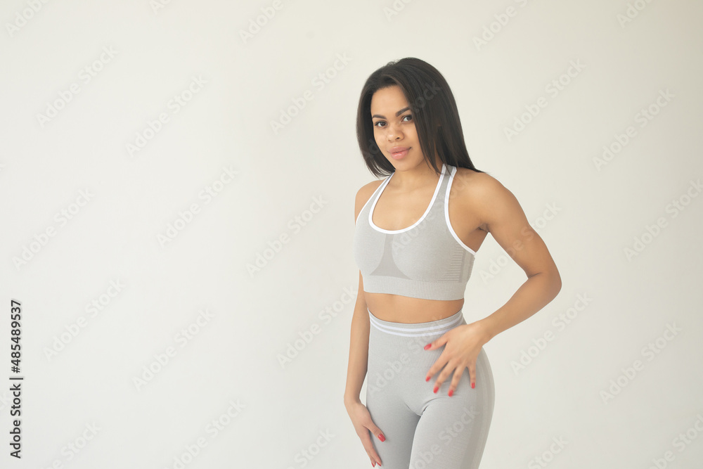 Full length of strong attractive african american sportswoman in sports bra and leggings standing over white background. Full length of strong attractive african american sportswoman in sports bra and leggings standing over white background.