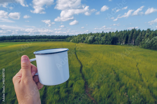 Enamel white mug mockup with path in the field grass background. Trekking merchandise and camping geer marketing photo. Stock wildwood photo with white metal cup. Rustic scene, producttemplate.