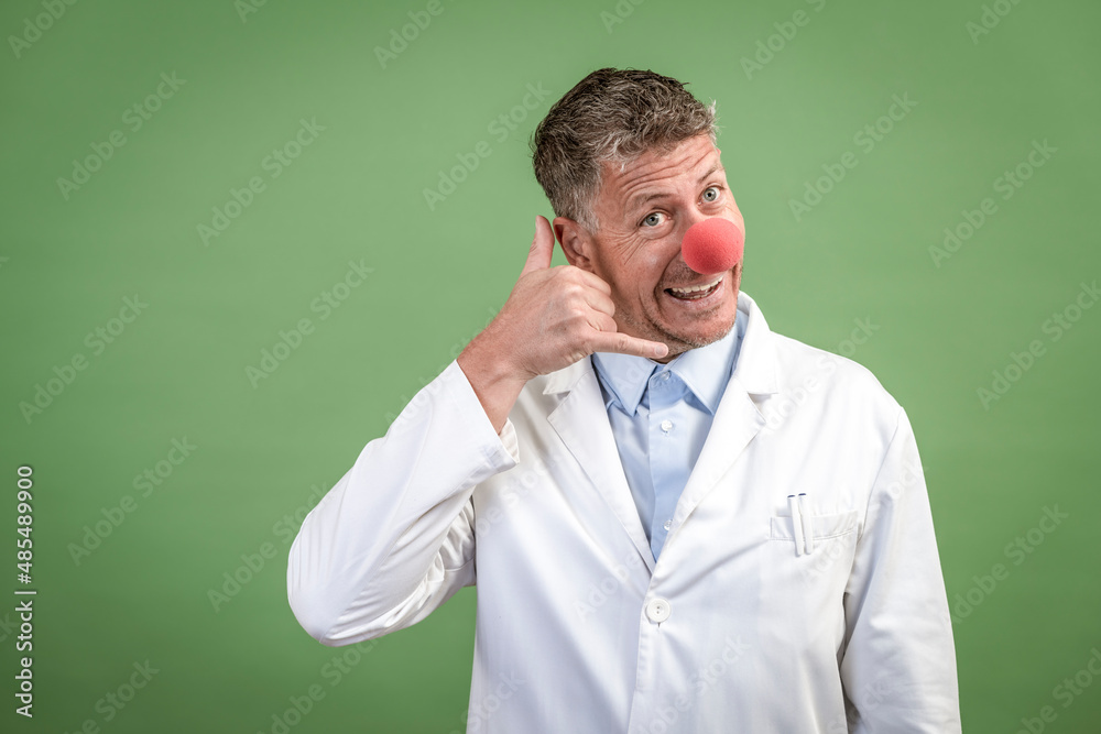 Scientist with white coat has red clown nose on and stands in front of green background Scientist with white coat has red clown nose on and stands in front of green background