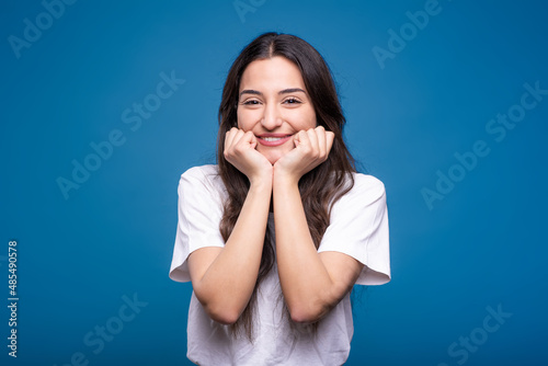 Portrait of happy and attractive caucasian or arab brunette girl in white t-shirt isolated on blue studio background.