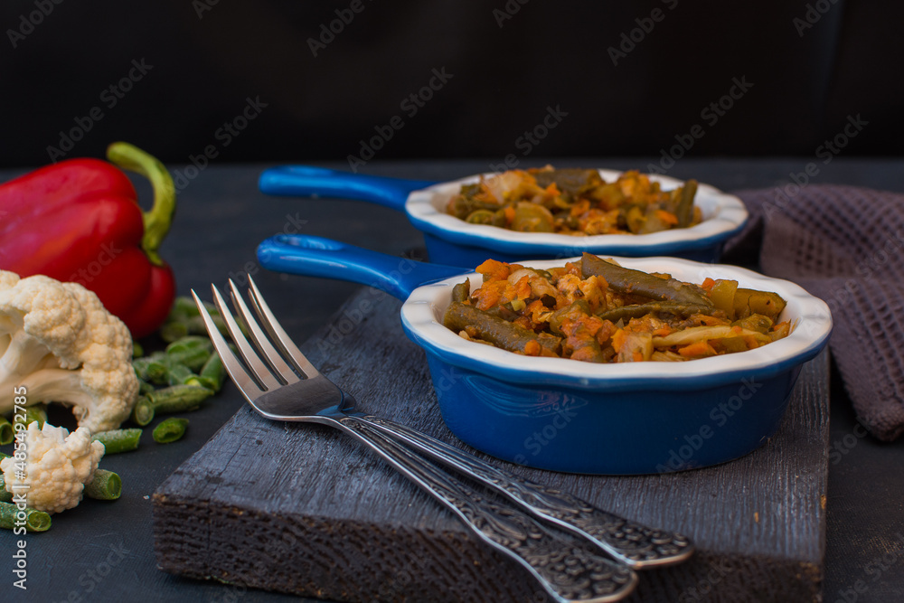 Vegetable stew with green beans and cauliflower and sweet peppers in a ceramic bowl on a wooden stand.
Vegetable stew with green beans and cauliflower and sweet peppers in a ceramic bowl on a wooden stand.