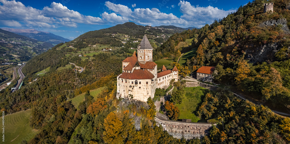 Val Isarco, Italy - Aerial panoramic view of Trostburg Castle (Castel Trostburg), a XII century fortress at the Italian Dolomites on a sunny autumn day with autumn foliage and blue sky with clouds