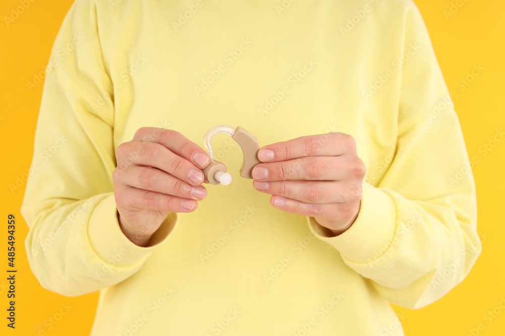 Fototapeta premium Woman holds hearing aid on yellow background