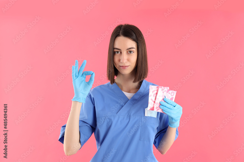 Female trainee nurse with pads and pregnancy test on pink background Female trainee nurse with pads and pregnancy test on pink background
