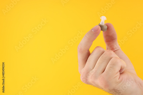 Male hand holds hearing aid on yellow background