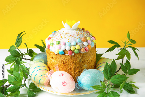 Easter cake with painted eggs on a platter in a white table. Traditional festive food. Yellow background photo