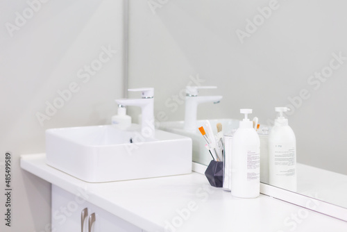 Cosmetic bottles and brushes are on the table near the sink in the white room. The interior of a bathroom or a medical office