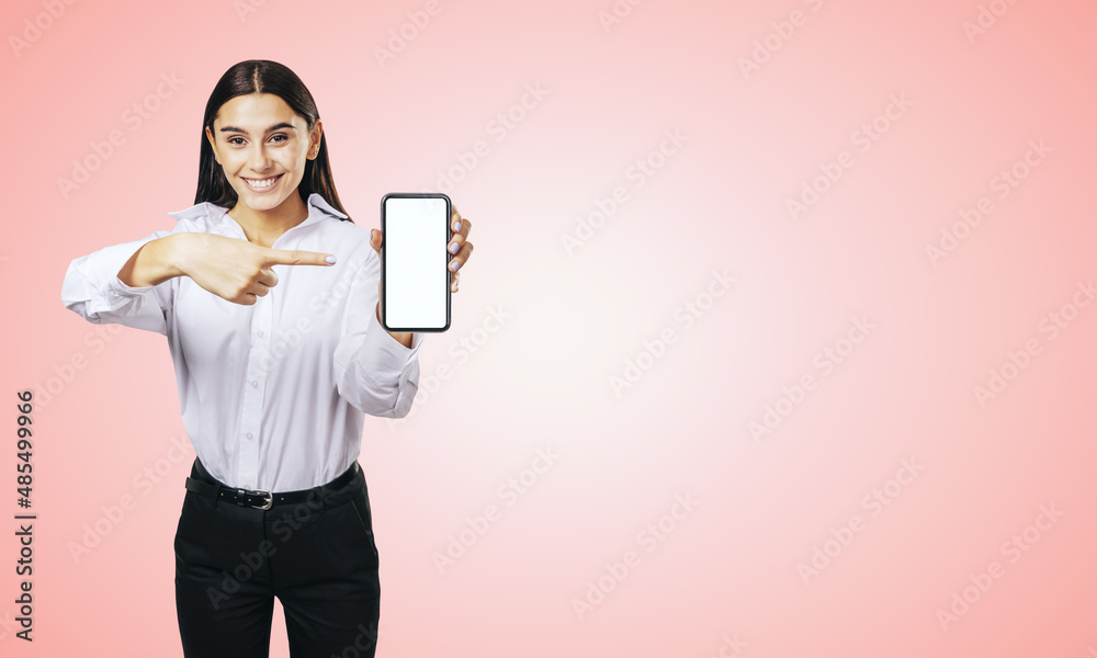 Mobile application concept with happy girl in white shirt showing modern smartphone with mockup blank white screen on abstract light pink background Mobile application concept with happy girl in white shirt showing modern smartphone with mockup blank white screen on abstract light pink background