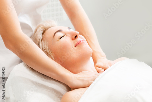 Portrait of an adult beautiful smiling woman at a massage session in a cosmetology clinic. The masseur performs the procedure on the neck and decollete area