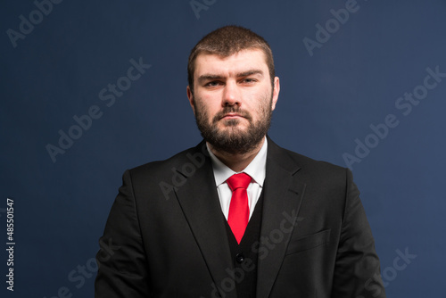A businessman is preparing for a business meeting. A man in a business suit with a red tie on a blue background looks confidently at the camera