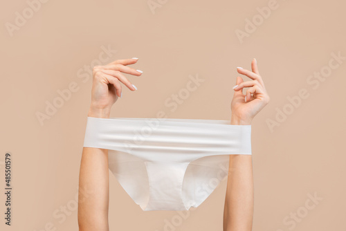 Elegant female hands with panties stretched over them. Beige background. Copy space. The concept of gynecology and depilation