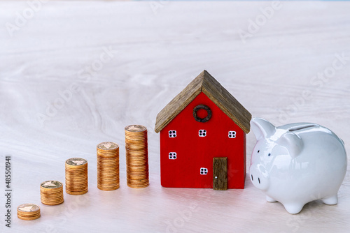 Piggy bank with stacks of coins are placed next to each other in a growing direction and many houses are placed on table, Saving money buy a house in the future and Investment real estate concept.