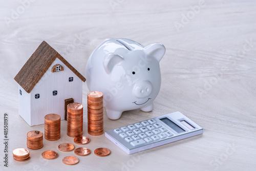 Piggy bank with the many stack gold coins with growth of value the benefit from dividends with calculator and home model  put on the table, Saving money buy home and Investment real estate concept.
