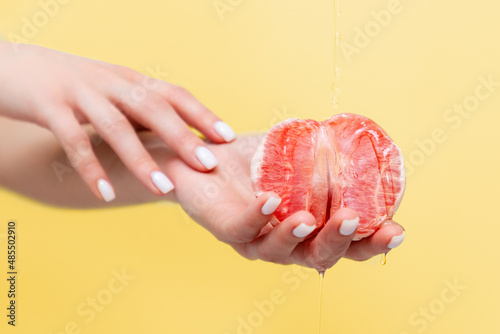 Female elegant hands hold half a grapefruit. Oil is poured on top of the fruit. Copy space. The concept of sexuality