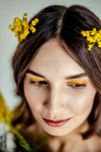 a close portrait of a girl with yellow shadows on her eyes and mimosa twigs in her light brown hair.