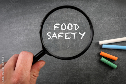Food Safety. Colored pieces of chalk and a magnifying glass on a dark chalkboard