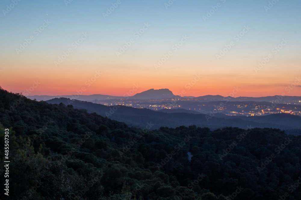 HDR shot of a Montserrat mountain viewed from far after the sunset where can be see the city lights around it.