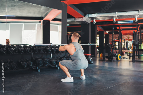 Athletic man trains in the gym, squating with a barbell. Back view. Keeping fit with cross training