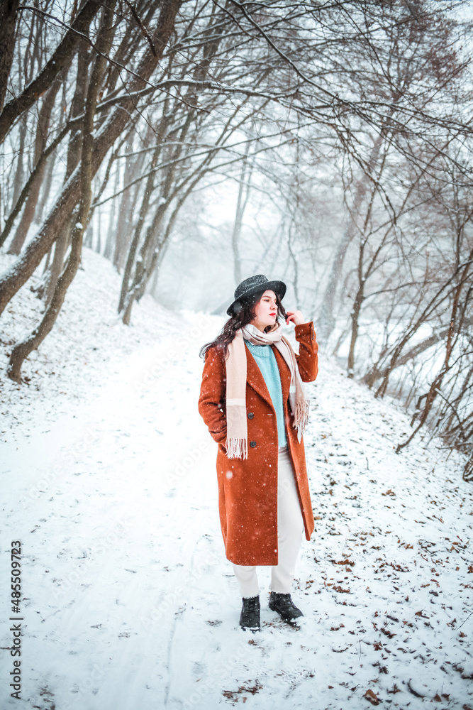 Beautiful woman standing among snowy trees in winter forest and enjoying first snow. Wearing hat, scarf and coat. Beautiful woman standing among snowy trees in winter forest and enjoying first snow. Wearing hat, scarf and coat.
