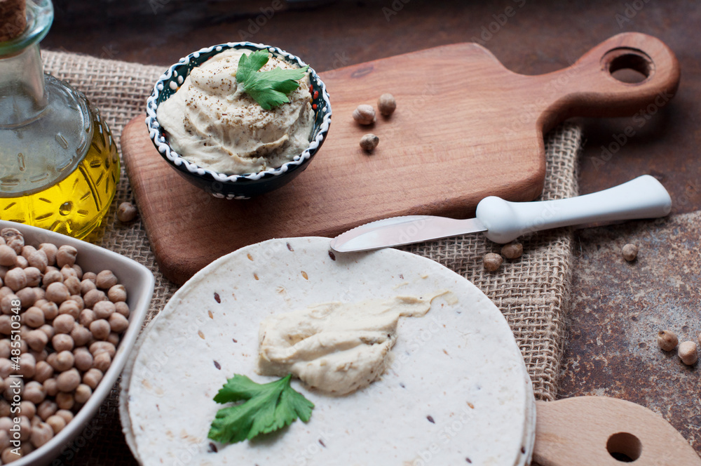 Hummus with parsley, olive oil, pita, chickpeas in a heart shaped bowl on canvas and dark brown background Hummus with parsley, olive oil, pita, chickpeas in a heart shaped bowl on canvas and dark brown background