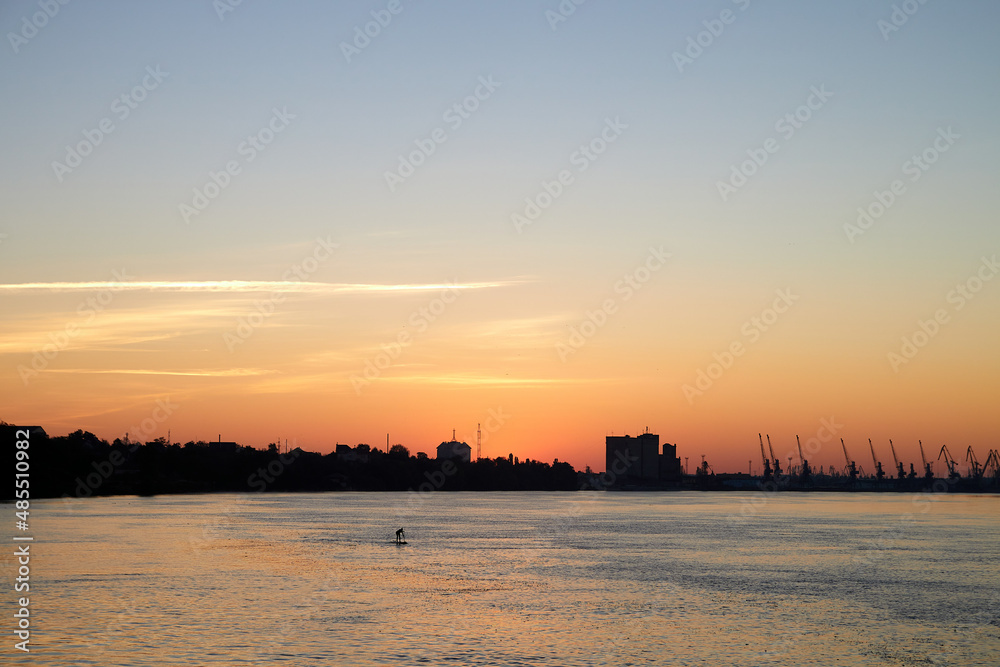 Silhouette of a young boy training on Stand Up Paddle Board, SUP at summer morning at the river