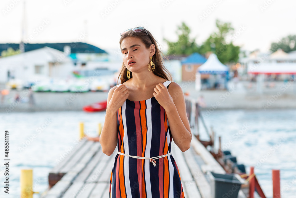 Summer. A tired woman holds on to the straps of her dress as she experiences heat stroke or faints. Outdoor. The concept of heat stroke and health problems